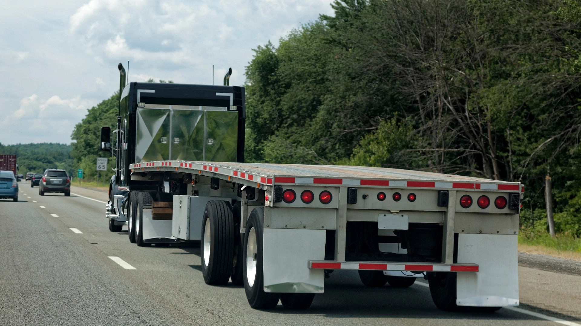 Black and white flatbed semi truck on highway with forest background